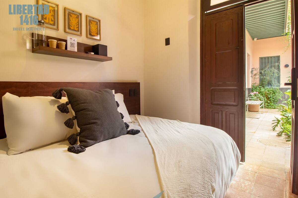 Hotelkamer met een bed, een houten hoofdbord, een plank met ingelijste foto’s en een deur naar een buitenruimte.