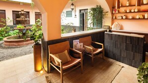 A reception area with a counter, two wooden chairs with cushions, a small rug, and a fountain in the background. - Hotel Libertad 1416 (Guadalajara)