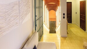A hallway with a sofa, a wall-mounted abstract art piece, and a door with illuminated panels. - Hotel Libertad 1416 (Guadalajara)