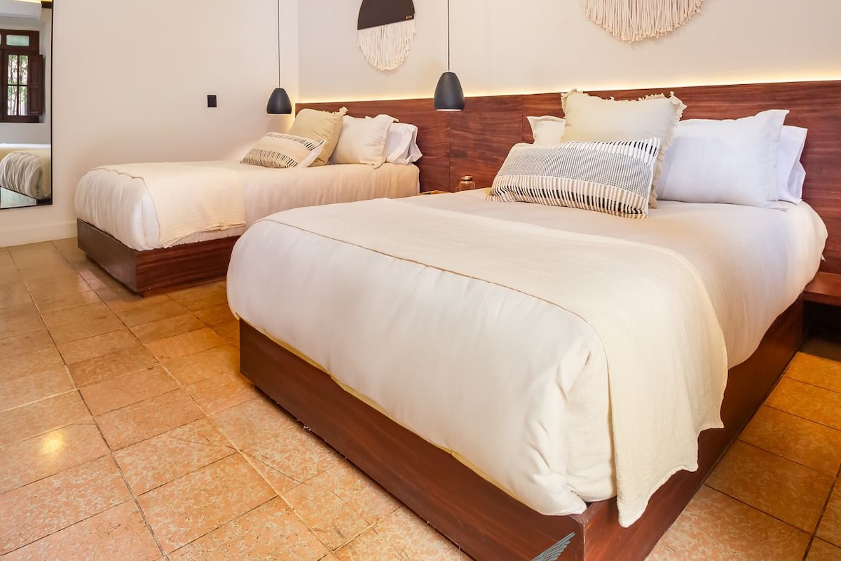 Habitación de hotel con dos camas, cabecera de madera y un espejo grande.