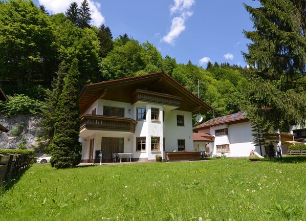A two-story building with a balcony, surrounded by a lush green lawn and trees.