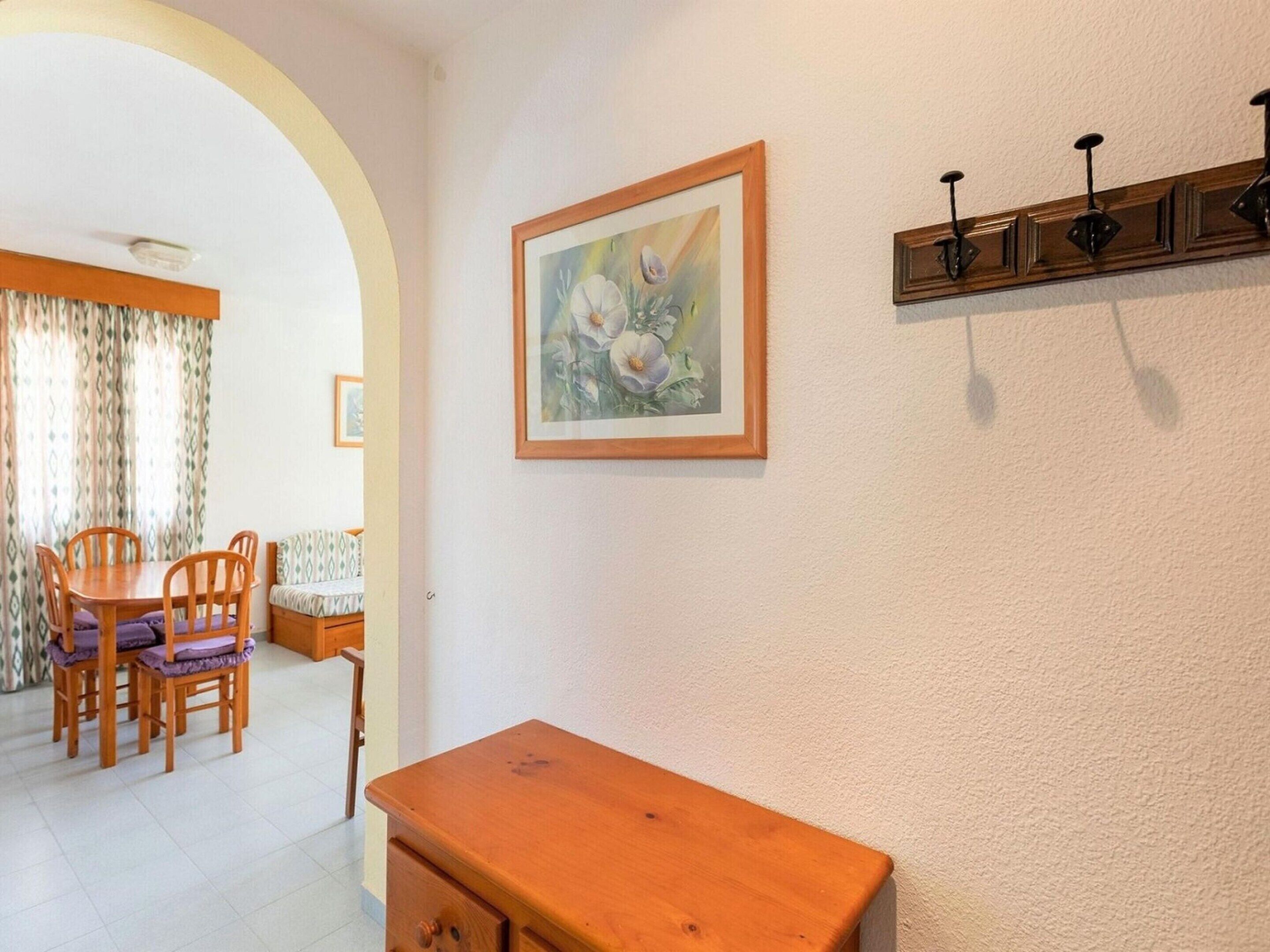 A dining area with a wooden table and chairs, a painting on the wall, and a wooden cabinet with hooks.