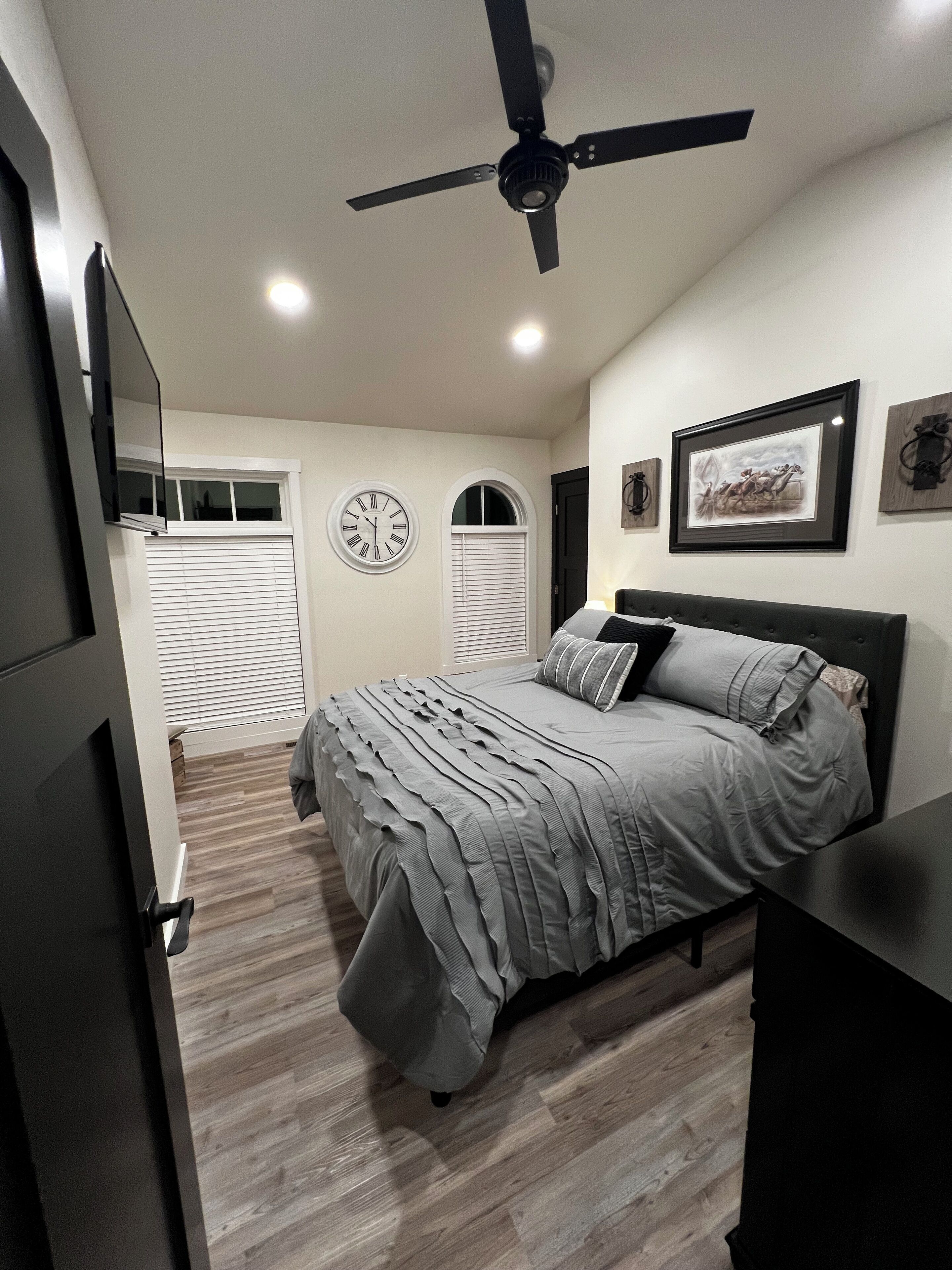 Un dormitorio con una cama, un ventilador de techo, un reloj y un cuadro en la pared.