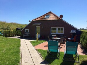 Ein Ziegelhaus mit einem Ziegeldach, eine kleine angebaute Garage und eine Terrasse mit zwei Stühlen und einem Tisch.