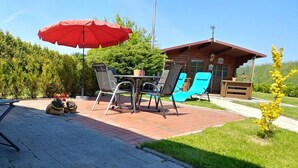 Une terrasse extérieure avec une table et des chaises, un parasol rouge et un bâtiment en bois en arrière-plan.