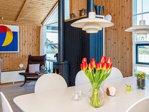 A modern interior with a dining table, chairs, a vase of tulips, a fireplace, and a large window. - 9 Person Holiday Home in Harboore (Harboore)