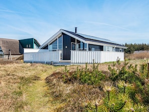 A modern house with a large deck, a chimney, and a thatched-roof structure in the background. - 9 Person Holiday Home in Harboore (Harboore)
