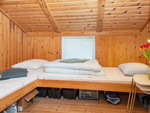 A small, wooden-paneled room with a bunk bed, a window with blinds, and a small table with a vase of flowers.