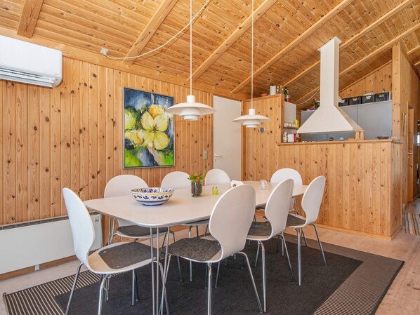 A wooden-paneled room with a dining table, chairs, a painting, and a kitchen area.