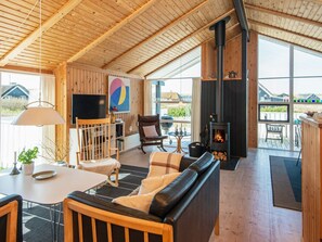A cozy cabin interior with a wooden ceiling, a fireplace, a sofa, a dining table, and a TV.
