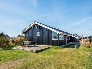 A black wooden house with a sloped roof, a wooden deck, and a small outdoor seating area.