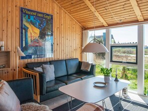 A modern living room with a wooden ceiling, a black leather sofa, a white table, and a poster of Vincent van Gogh's Café de Nuit. - 9 Person Holiday Home in Harboore (Harboore)
