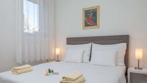 Un lit bien fait, avec du linge de lit blanc et deux serviettes pliées, une table de chevet avec une lampe et un tableau accroché au mur.