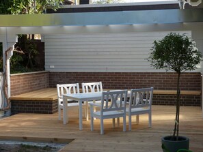 A patio with a wooden deck, white outdoor furniture, and a potted plant.