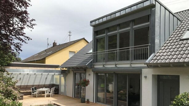 A modern house with a large deck, a small garden pond, and a dining area.