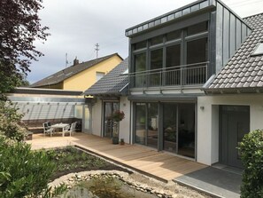 A modern house with a large deck, a small garden pond, and a dining area.