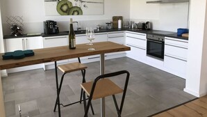 A modern kitchen with white cabinets, a wooden countertop, and a built-in oven. There are two stools and a wine bottle on the counter.