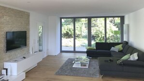 A modern living room with a flat-screen TV mounted on a brick wall, a dark-colored sofa with green cushions, and a glass coffee table.