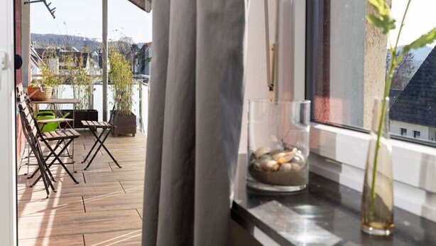 A balcony with a wooden floor, a table with chairs, a potted plant, and a vase with a flower. - Fewo Freiken 28 Comfortable Holiday Residence (Arnsberg)
