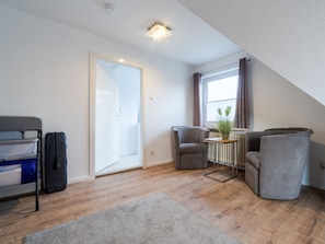 A modern, compact living space with a loft bed, two armchairs, a small table with a plant, and a large window with curtains. - Liam Comfortable Holiday Residence (Büsum)