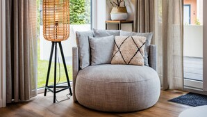 A modern living room with a round grey sofa, a woven floor lamp, and a potted plant on a shelf. - Lovely Holiday Home in Voorhuizen With Garden (Voorthuizen)