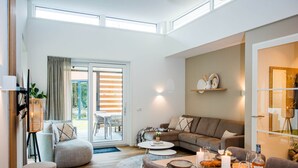 A modern living room with a sofa, dining table set for two, and a sliding glass door leading to an outdoor area. - Lovely Holiday Home in Voorhuizen With Garden (Voorthuizen)