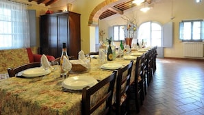 A dining area with a long table set for a meal, wooden chairs, and a high ceiling with exposed beams. - Elegant Castle Stay With Pool (Foiano della Chiana)