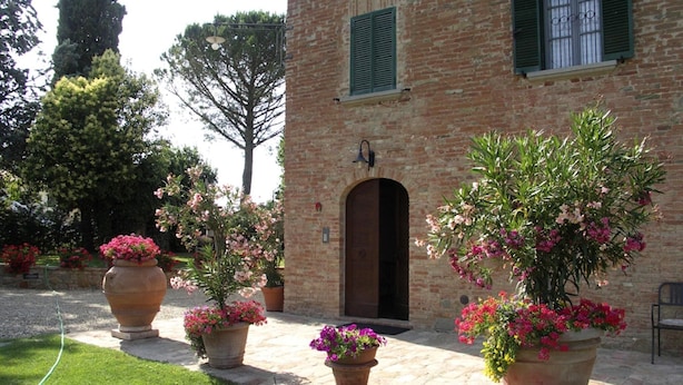 A brick building with an arched entrance, surrounded by potted plants with pink flowers. - Elegant Castle Stay With Pool (Foiano della Chiana)