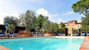A swimming pool with lounge chairs and umbrellas, surrounded by trees and a building. - Elegant Castle Stay With Pool (Foiano della Chiana)