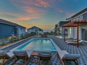 A swimming pool with lounge chairs and a pergola, surrounded by modern buildings and a sunset sky. - Apartment in Croatia Near the Adriatic Coast (Sukosan)
