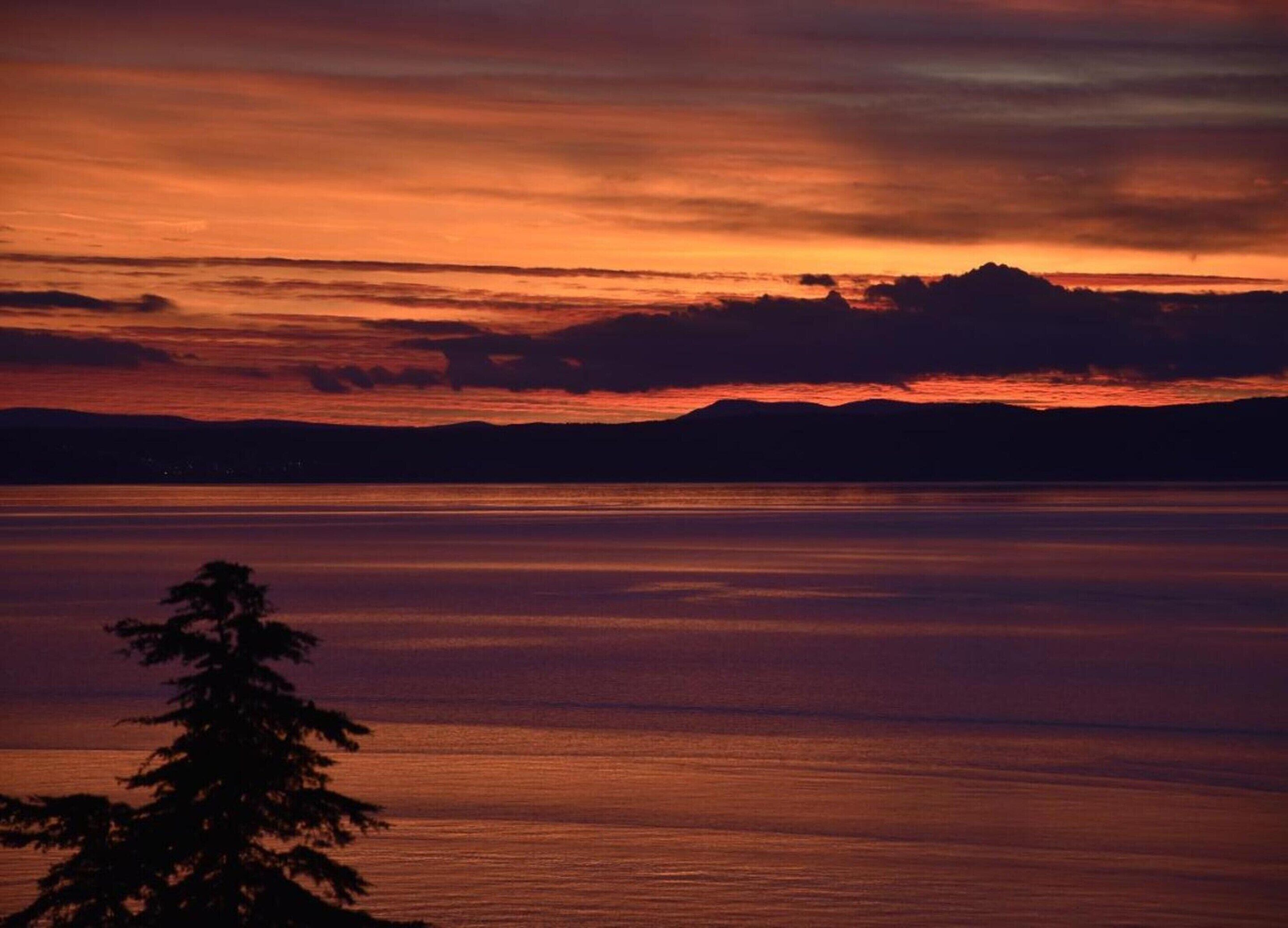 A sunset over a calm body of water with a silhouette of a mountain range in the distance.