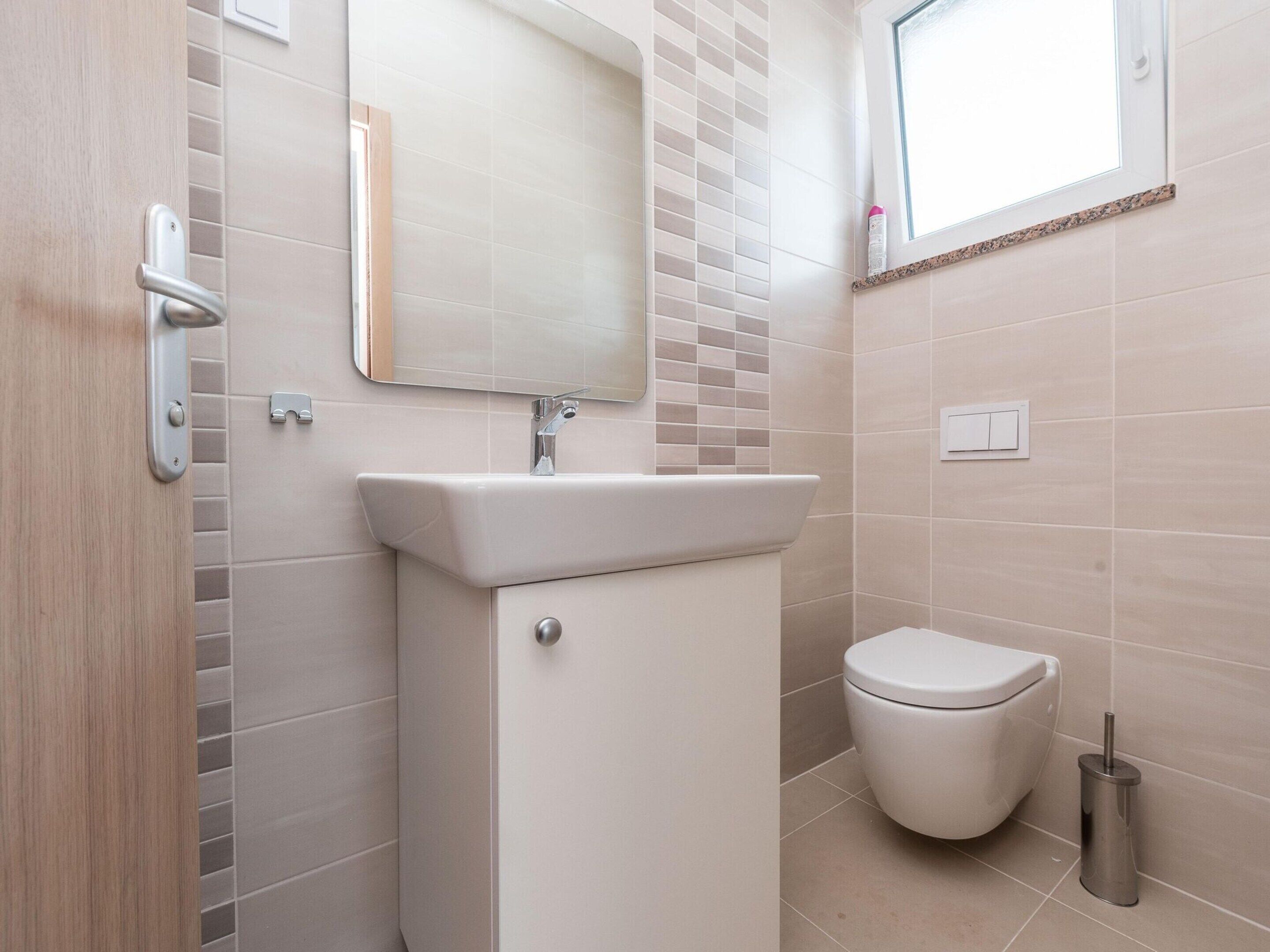 Une salle de bain avec un lavabo blanc, un miroir, des toilettes et une fenêtre.