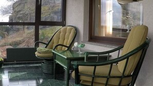 A room with two green wicker chairs, a small table, and a view of a rocky landscape through large windows. - Uitzicht op Droomlocatie (Annaberg-Buchholz)