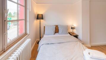 Een slaapkamer met een bed, twee bedlampen, een raam met uitzicht en een radiator.