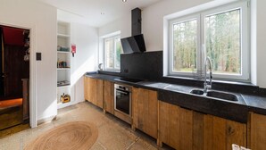 A modern kitchen with wooden cabinets, a black countertop, and a built-in oven. There are two windows providing natural light and a view of the outdoors. - Luxury Chalet in Jalhay With Private Sauna (Jalhay)