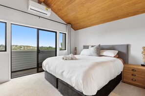 Ein Schlafzimmer mit einem großen Bett, einem Nachttisch aus Holz und Blick durch eine Schiebetür.