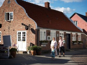A brick building with a sloped roof, a sign reading "Sisters," and a small outdoor seating area with chairs and potted plants.