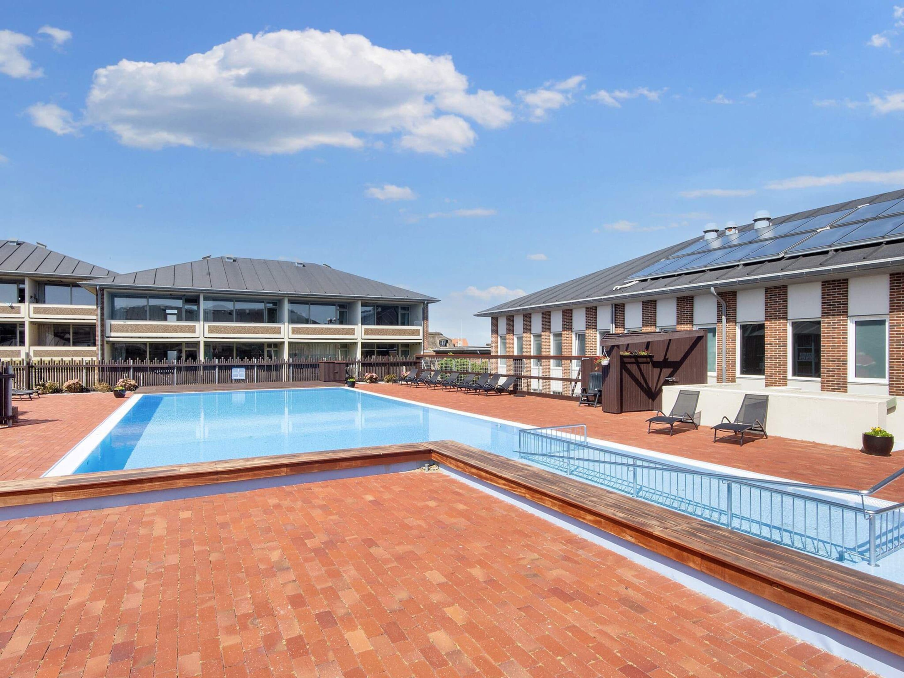 A rooftop pool area with a clear blue sky, a brick patio, and lounge chairs.