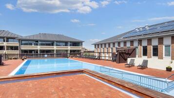 A rooftop pool area with a clear blue sky, a brick patio, and lounge chairs.