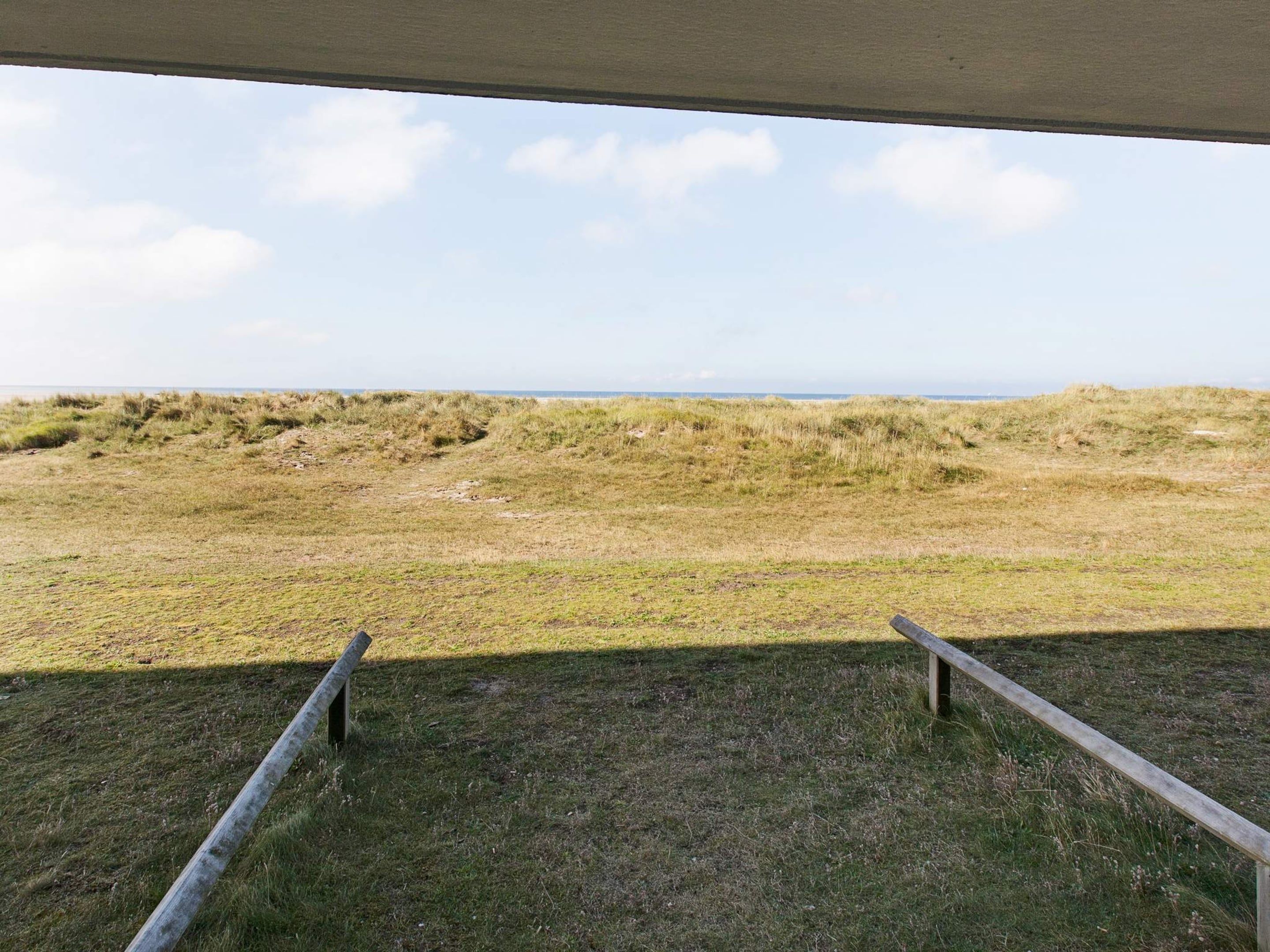 A view from a covered area overlooking a grassy field with a distant horizon.