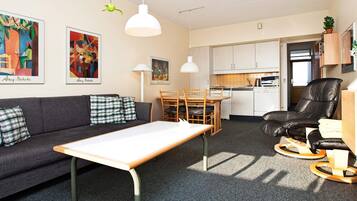 A compact living space with a sofa, a dining table, a kitchen area, and a black leather chair.
