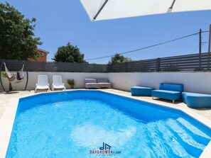 A swimming pool with white lounge chairs and blue sofas, surrounded by a white wall and a black fence. - Villa Kostre Comfortable Holiday Residence (Marcana)