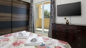 Une chambre à coucher comprenant un lit, une télévision, une commode et une porte coulissante donnant sur un balcon.