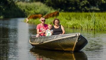 Ein schmaler Kanalboot mit drei Personen auf einem ruhigen Fluss, umgeben von viel Grün.