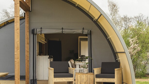 A semi-open tent with two wooden chairs and a small table, a wooden deck, and a view of the interior through a doorway.
