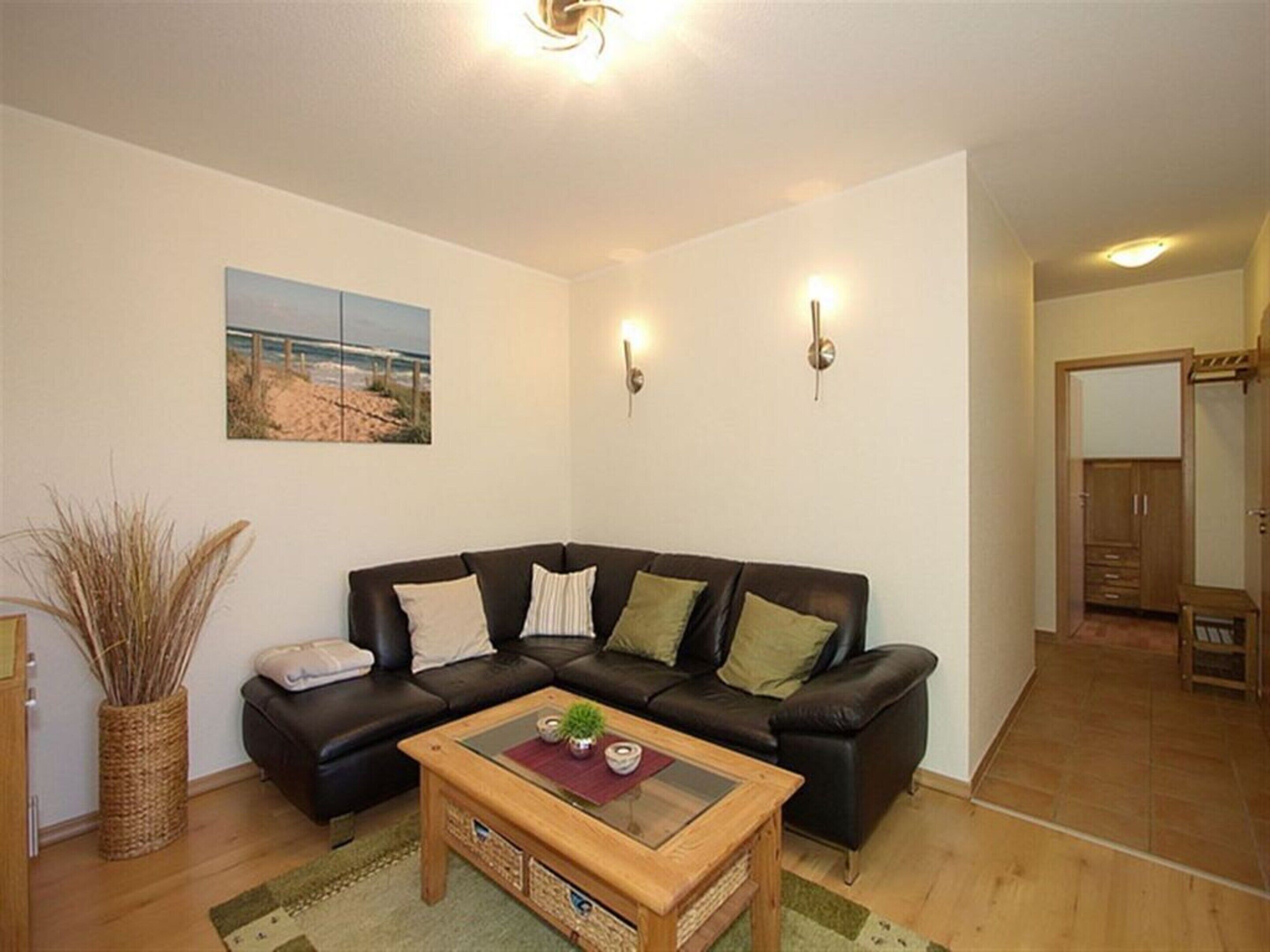 A living room with a black leather sofa, a wooden coffee table, a woven basket, and a painting of a beach scene.