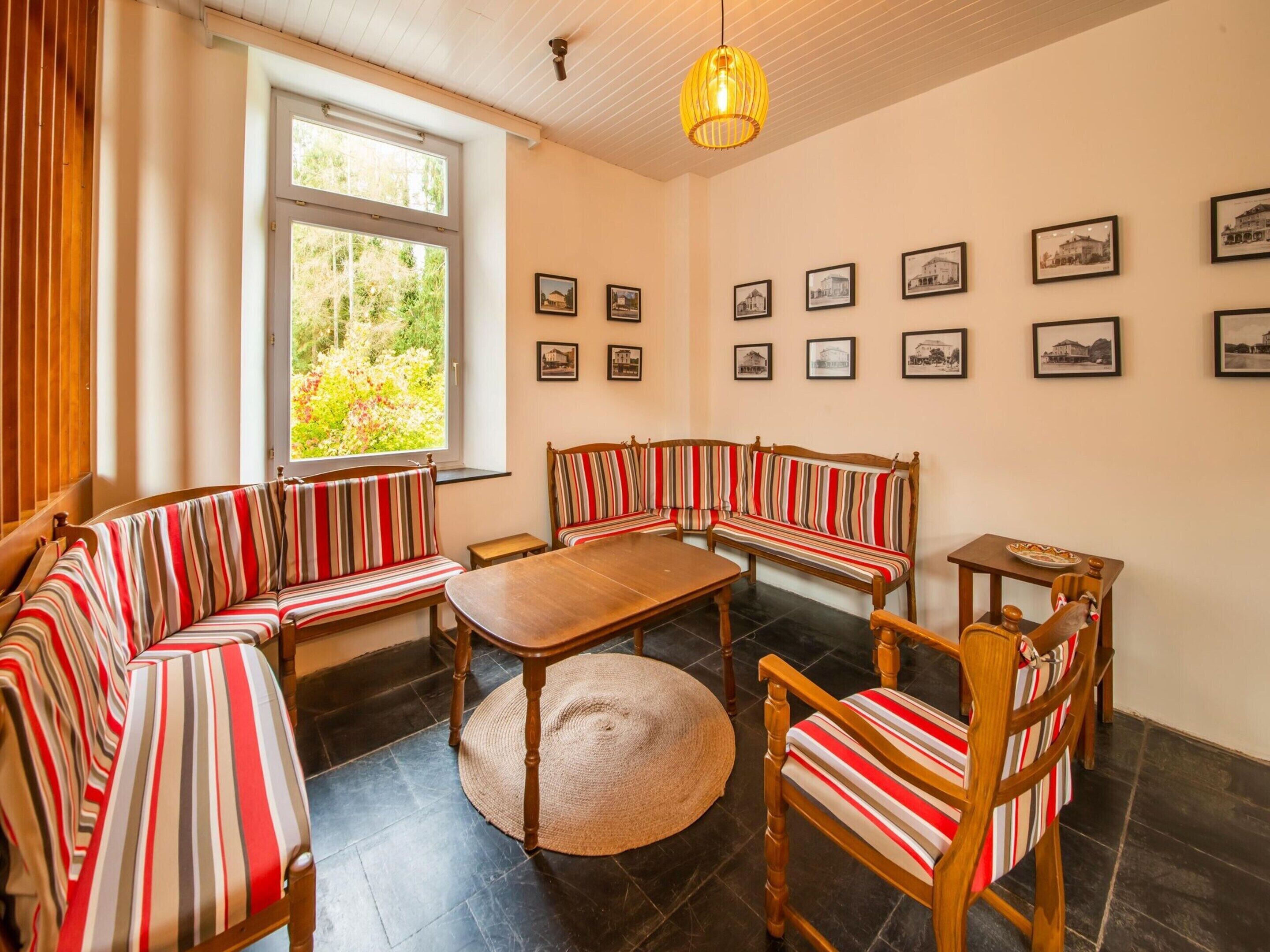 Een gezellige kamer met gestreepte banken, een houten tafel en een groot raam met uitzicht op groen.