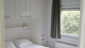 A bedroom with a bed, a wardrobe, a window with curtains, and a view of greenery outside. - Cosy Holiday Home in Appelscha With a Great View (Appelscha)