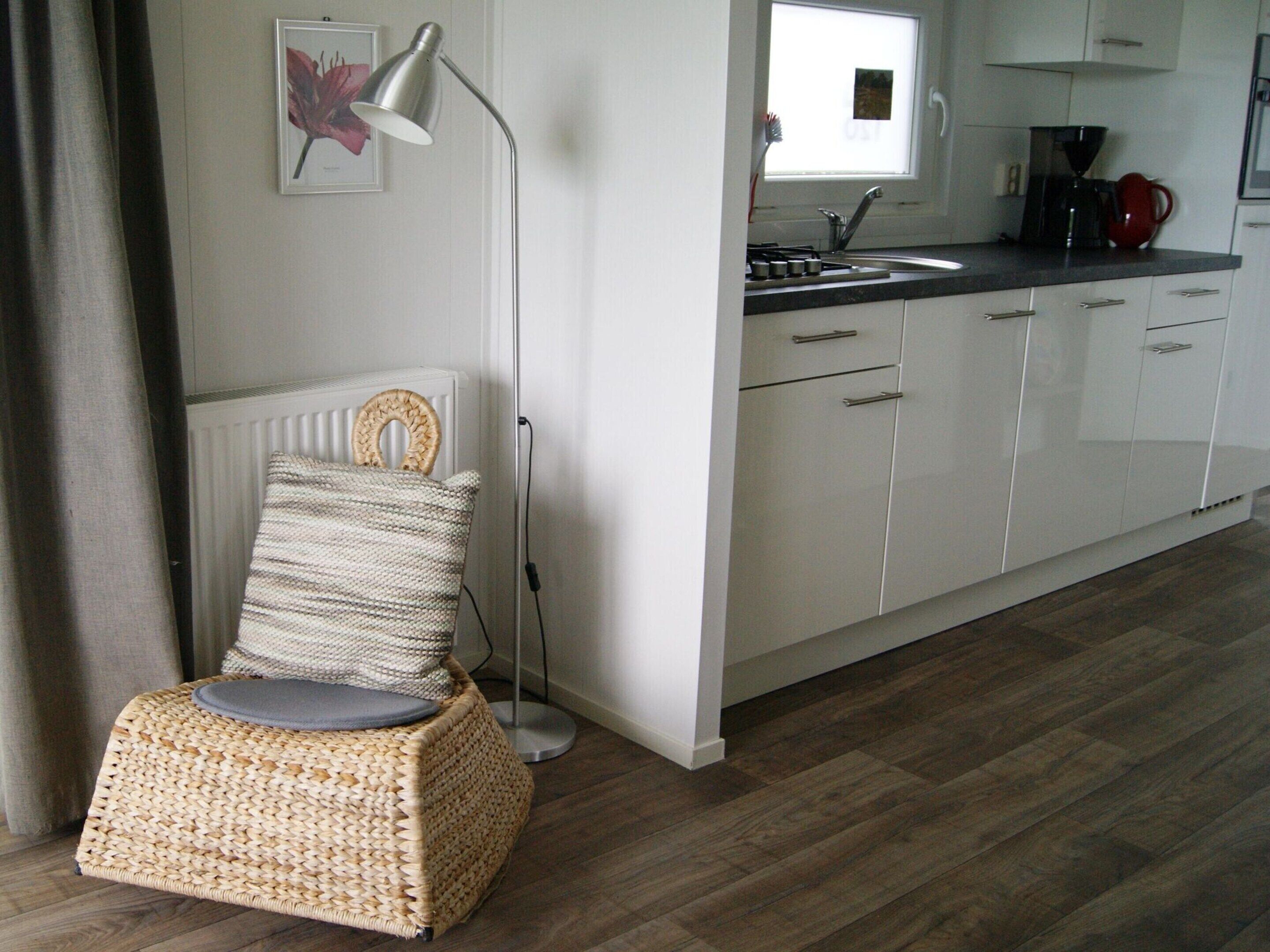 A kitchen with white cabinets, a black countertop, and a wicker chair with a cushion. - Cosy Holiday Home in Appelscha With a Great View (Appelscha)