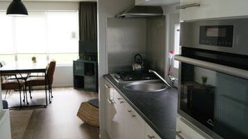 Een moderne keuken met een fornuis, spoelbak en magnetron. Er is een eethoek met een tafel en stoelen.